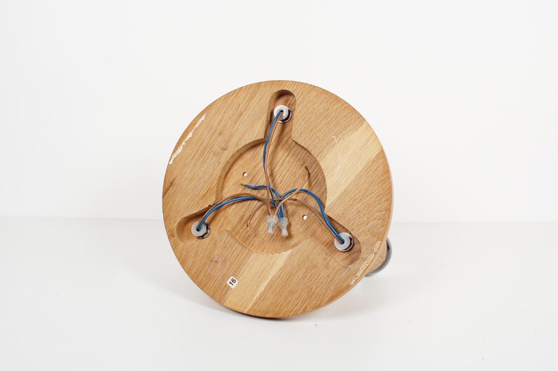 May include: A round, wooden light fixture base with visible wood grain. The base has three holes with wires and a central recessed area. Blue and brown wires are visible. The fixture is set against a white background.