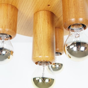 K&ouml;nnte beinhalten: Eine Deckenleuchte aus Holz mit vier Gl&uuml;hbirnen. Die Leuchte ist aus Naturholz gefertigt und hat einen runden Sockel. Die Gl&uuml;hbirnen sind aus klarem Glas mit silberner Oberfl&auml;che.