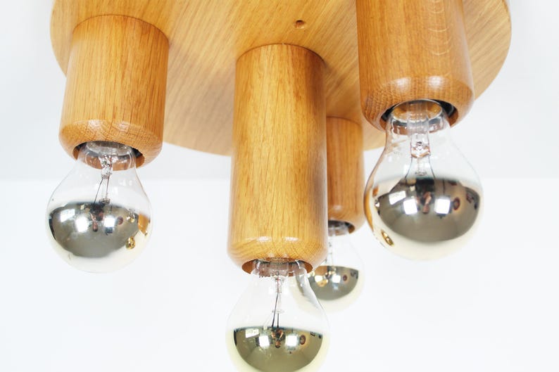 K&ouml;nnte beinhalten: Eine Deckenleuchte aus Holz mit vier Gl&uuml;hbirnen. Die Leuchte ist aus Naturholz gefertigt und hat einen runden Sockel. Die Gl&uuml;hbirnen sind aus klarem Glas mit silberner Oberfl&auml;che.