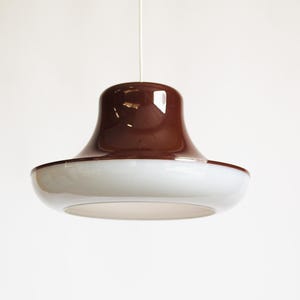 May include: A modern pendant light fixture with a brown top and a white, rounded bottom. The light hangs from a thin white cord against a plain white background. The fixture has a glossy finish.