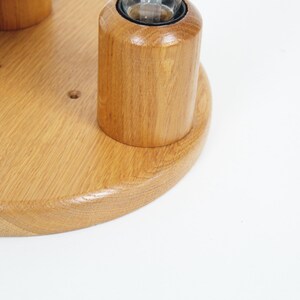 May include: A wooden candle holder with a light brown finish. The holder has a circular base and several cylindrical sections designed to hold candles. The wood grain is visible, and the design is simple and elegant.