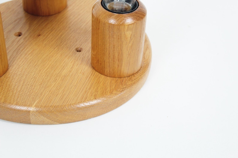 May include: A wooden candle holder with a light brown finish. The holder has a circular base and several cylindrical sections designed to hold candles. The wood grain is visible, and the design is simple and elegant.