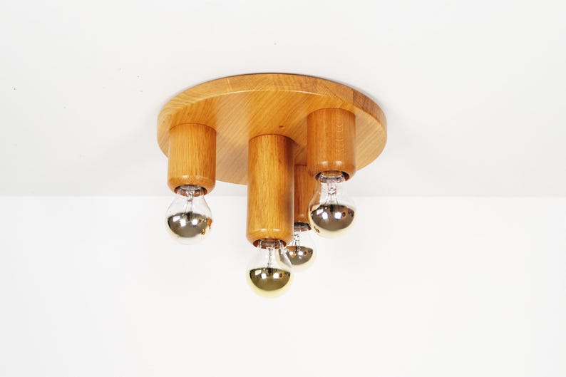 K&ouml;nnte beinhalten: Eine Deckenleuchte aus Holz mit vier Gl&uuml;hbirnen. Die Leuchte ist rund mit einem Holzsockel und vier Holzzylindern, die die Gl&uuml;hbirnen halten.