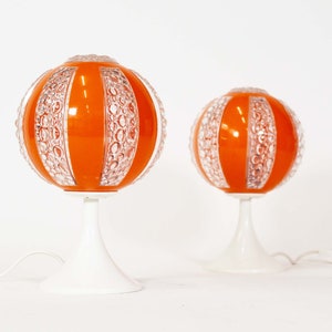 May include: Two orange and white globe table lamps with a textured glass shade. The lamps have a white base and a white cord.