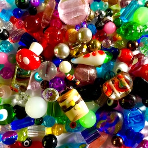 May include: A large assortment of colourful glass beads, including clear, blue, green, red, and purple beads. There are also some white and black beads, as well as some beads with unique designs.