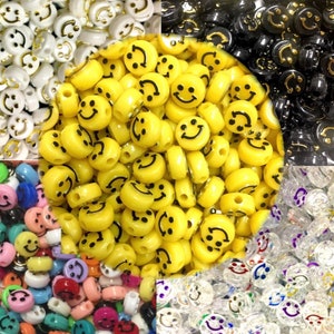 May include: A close-up of a selection of smiley face beads in yellow, black and white. The beads are made of plastic and have a glossy finish. They are ideal for making jewellery, crafts and other projects.