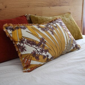 Peut inclure: Un lit blanc avec un oreiller à motifs jaunes, orange et bruns avec une bordure à franges. L'oreiller est posé sur un oreiller rouge et un oreiller doré.