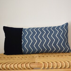 Peut inclure: Un coussin lombaire bleu et blanc à motifs avec un dos en velours noir. Le coussin est posé sur un banc en osier tressé.