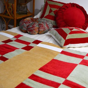 Può includere: Un letto con un piumone a quadri color tan, rosso e verde. Ci sono tre cuscini decorativi sul letto, un cuscino rotondo rosso, un cuscino con motivi verdi e rossi e un cuscino geometrico verde e rosso.