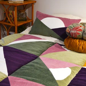 Op de afbeelding: Een patchworkdeken met geometrische vormen in tinten groen, paars, roze en wit. De deken is gemaakt van corduroy stof en heeft een casual, moderne stijl.