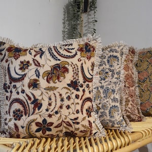 May include: Three decorative throw pillows with a floral pattern in shades of blue, red, and brown. The pillows have a white background and a fringe trim.