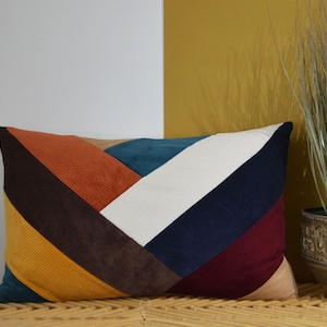 Peut inclure: Un coussin rectangulaire avec un motif géométrique dans des tons de bleu sarcelle, orange, marron, blanc, bleu marine et bordeaux. Le coussin est en tissu de velours côtelé.