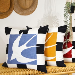 Peut inclure: Trois coussins décoratifs avec un motif à carreaux noirs et blancs. Chaque coussin présente une silhouette blanche d'une hirondelle sur un fond coloré. Les coussins sont bleus, jaunes et rouges.