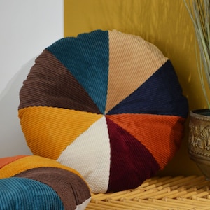 Può includere: Cuscino rotondo in velluto a coste con un design circolare. Il cuscino è realizzato in otto diversi colori di velluto a coste, tra cui verde acqua, beige, marrone, blu navy, giallo, bianco, rosso e arancione.