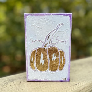 May include: A small, white canvas painting with a purple border. The painting features a gold pumpkin with the word "WORD" written on it.
