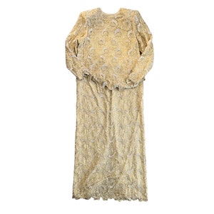May include: A long, ivory-coloured lace dress with a ruffled neckline and long sleeves. The dress is made of delicate lace with a floral pattern.