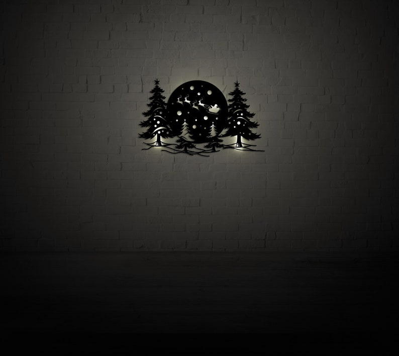 K&ouml;nnte beinhalten: Schwarze Wandkunst aus Metall, die eine Winterszene mit drei B&auml;umen und einem Vollmond darstellt. Der Weihnachtsmann fliegt in einem von Rentieren gezogenen Schlitten durch die Luft. Schneeflocken fallen vom Himmel.