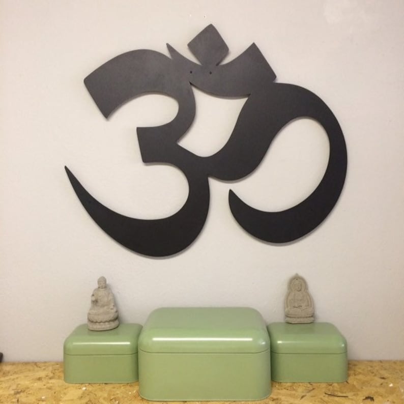 May include: A black metal Om symbol wall decor with two small grey Buddha statues on green boxes.