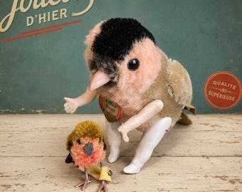 Könnte beinhalten: Ein Plüschvogel-Spielzeug im Vintage-Stil mit schwarzer Kappe, rosig-beigem Körper und beweglichen weißen Kunststoffarmen und -beinen, begleitet von einer kleineren, flauschigen braun-orangen Vogelfigur mit dünnen Drahtbeinen.