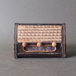 May include: A vintage wooden radio with a woven wicker front panel. The radio has three round knobs and a blue and white label.