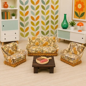 May include: A miniature dollhouse living room set featuring a two-seat sofa and two matching armchairs upholstered in a beige fabric with a yellow and blue floral pattern and gold fringe trim, arranged around a small dark brown wooden coffee table.