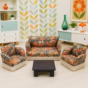 May include: A miniature dollhouse living room set featuring a sofa and two armchairs upholstered in a floral fabric with orange, blue, and green tones, accented with cream-colored fringe trim, paired with a small, dark brown square wooden coffee table.