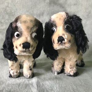 K&ouml;nnte beinhalten: Zwei Pl&uuml;schhunde mit cremefarbenem und schwarzem Fell mit dunklen Flecken. Jedes Stofftier hat lange, herabh&auml;ngende schwarze Ohren, eine schwarze gestickte Nase und gro&szlig;e Wackelaugen aus Kunststoff. Die Hunde stehen nebeneinander.