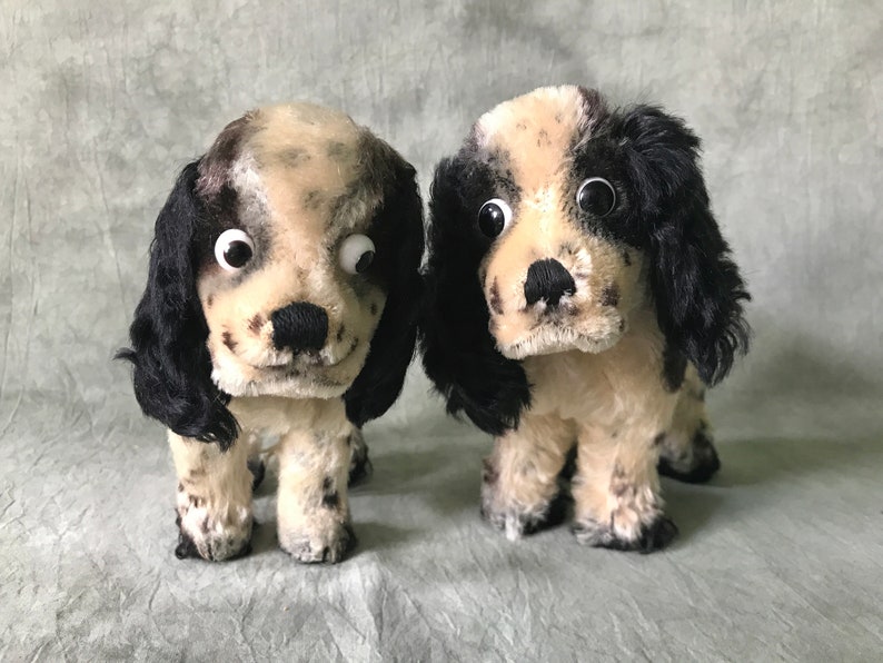 K&ouml;nnte beinhalten: Zwei Pl&uuml;schhunde mit cremefarbenem und schwarzem Fell mit dunklen Flecken. Jedes Stofftier hat lange, herabh&auml;ngende schwarze Ohren, eine schwarze gestickte Nase und gro&szlig;e Wackelaugen aus Kunststoff. Die Hunde stehen nebeneinander.