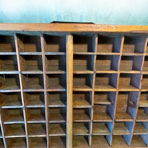 May include: A vintage wooden organizer with numerous small compartments. The organizer is constructed from light-colored wood and features a grid-like structure with multiple rectangular spaces. The compartments are arranged in rows and columns, creating a storage solution.