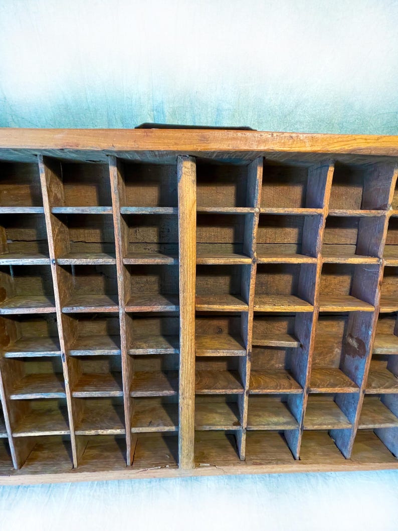 May include: A vintage wooden organizer with numerous small compartments. The organizer is constructed from light-colored wood and features a grid-like structure with multiple rectangular spaces. The compartments are arranged in rows and columns, creating a storage solution.
