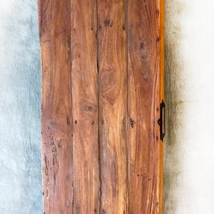 May include: A rectangular wooden serving tray with a dark handle and a metal handle. The tray is made of vertical wooden planks with visible wood grain and is stained a warm brown color. The tray has a rustic, handcrafted appearance.