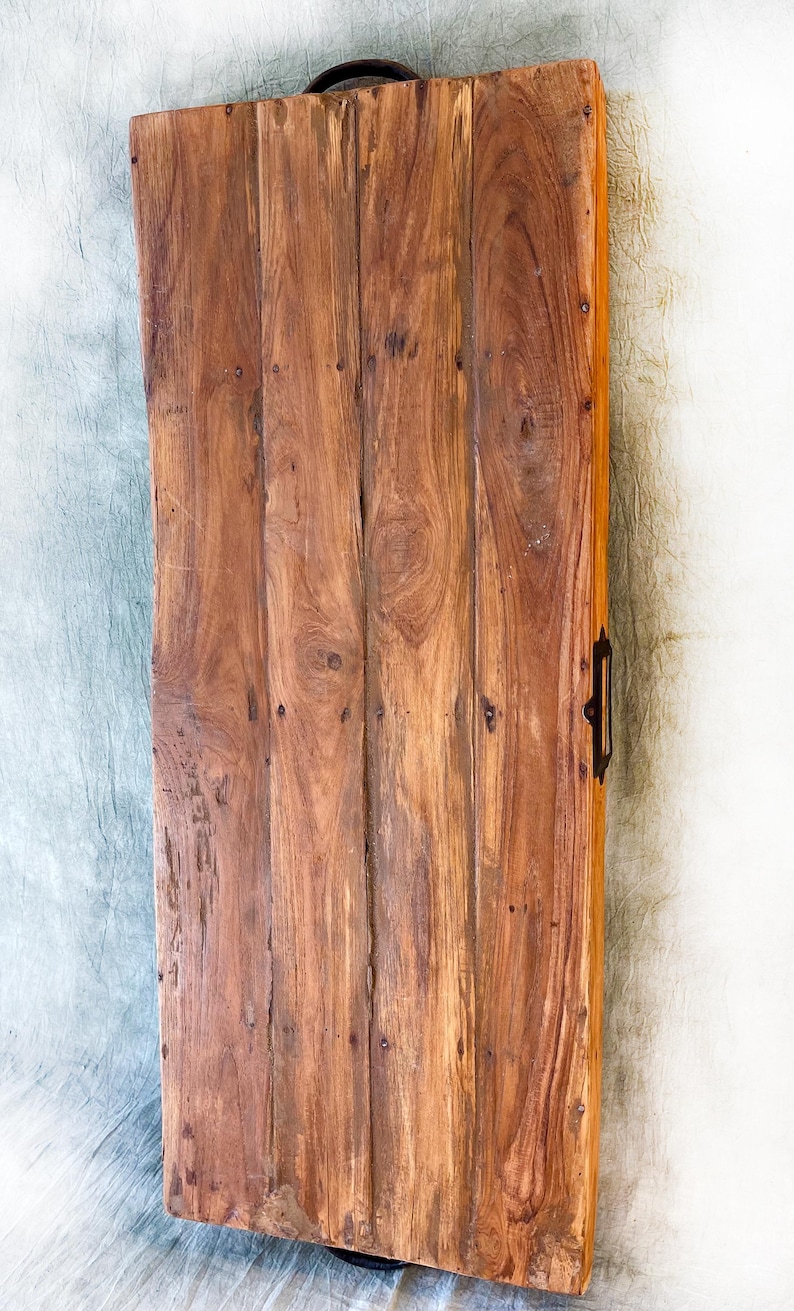May include: A rectangular wooden serving tray with a dark handle and a metal handle. The tray is made of vertical wooden planks with visible wood grain and is stained a warm brown color. The tray has a rustic, handcrafted appearance.