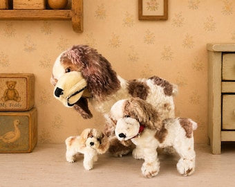 May include: Three plush spaniel dog toys in varying sizes, featuring white fur with brown patches, floppy ears, and black noses. The medium-sized dog wears a red collar with a small bell. The toys have a soft, textured appearance.