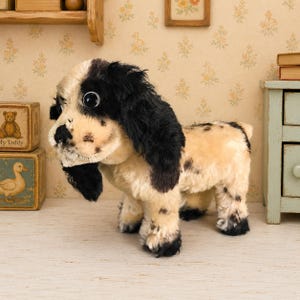 May include: A plush toy dog with cream-colored fur and black patches on its ears, face, and body. The stuffed animal features large, round, dark plastic eyes, a black nose, and long, floppy ears. It stands on four legs in a realistic pose.