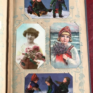 May include: A vintage photo album with four different images of children. The first image shows two children in winter clothing on a sled. The second image shows a girl holding a bouquet of pink roses. The third image shows a girl in a traditional dress holding a bouquet of lavender. The fourth image shows three children in winter clothing on a sled.