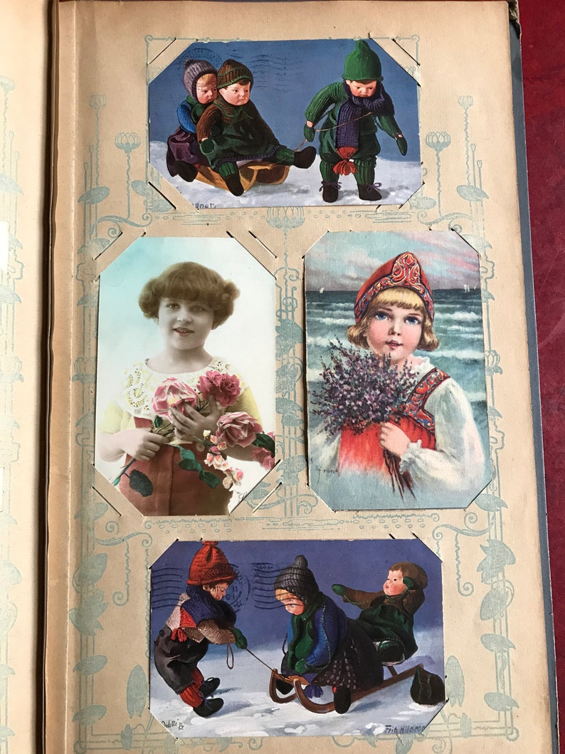 May include: A vintage photo album with four different images of children. The first image shows two children in winter clothing on a sled. The second image shows a girl holding a bouquet of pink roses. The third image shows a girl in a traditional dress holding a bouquet of lavender. The fourth image shows three children in winter clothing on a sled.