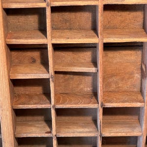 May include: A close-up of a vintage wooden printer's tray with multiple small compartments. The tray is made of light brown wood and has a grid-like structure. The compartments are empty and ready for use.