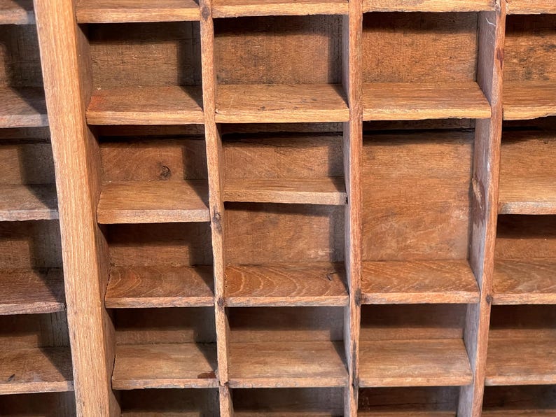 May include: A close-up of a vintage wooden printer's tray with multiple small compartments. The tray is made of light brown wood and has a grid-like structure. The compartments are empty and ready for use.