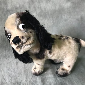 K&ouml;nnte beinhalten: Ein Pl&uuml;schhund mit schwarz-wei&szlig; geflecktem Fell, langen, herabh&auml;ngenden schwarzen Ohren und auff&auml;lligen wei&szlig;en Wackelaugen aus Kunststoff. Das Stofftier hat eine schwarze, gestickte Nase und einen strukturierten, flauschigen K&ouml;rper mit kurzem Schwanz.