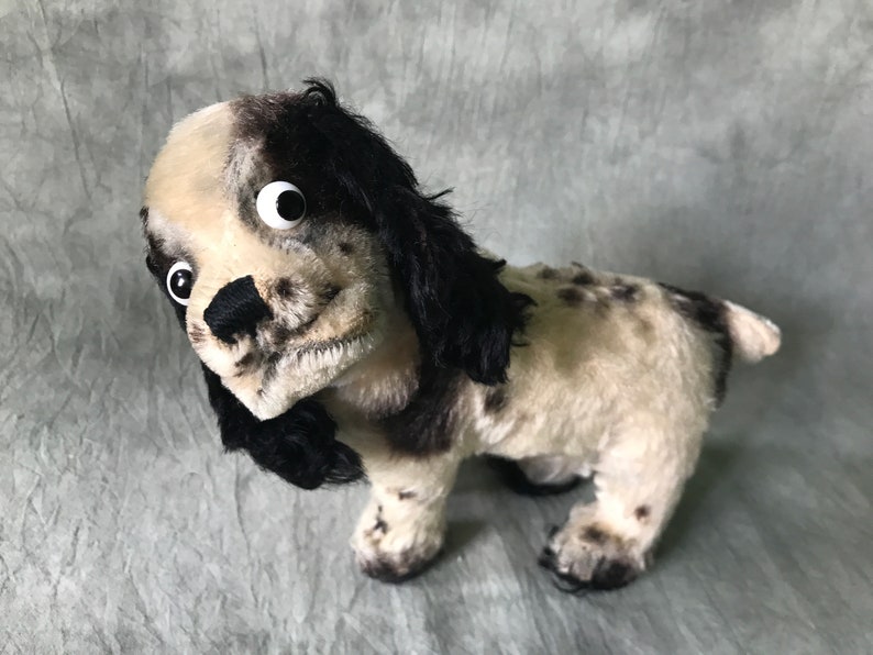 K&ouml;nnte beinhalten: Ein Pl&uuml;schhund mit schwarz-wei&szlig; geflecktem Fell, langen, herabh&auml;ngenden schwarzen Ohren und auff&auml;lligen wei&szlig;en Wackelaugen aus Kunststoff. Das Stofftier hat eine schwarze, gestickte Nase und einen strukturierten, flauschigen K&ouml;rper mit kurzem Schwanz.