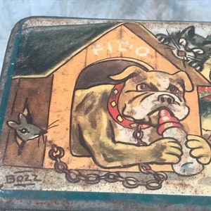 Puede incluir: Caja de hojalata vintage con una ilustración colorida de un bulldog llamado Fido en una caseta, un gato, un ratón y un pato. La caja tiene un fondo verde y el texto "BOLL" es visible.
