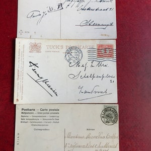 May include: Three vintage postcards with handwritten messages. The top postcard has a red stamp with the text "POSTZEGE BOVEN IN VLUGGER VERZENDING". The middle postcard has a red stamp with the text "TUCK'S POSTKARTE". The bottom postcard has a red stamp with the text "MALINES STATION 26 JUILLET 10-11 107".