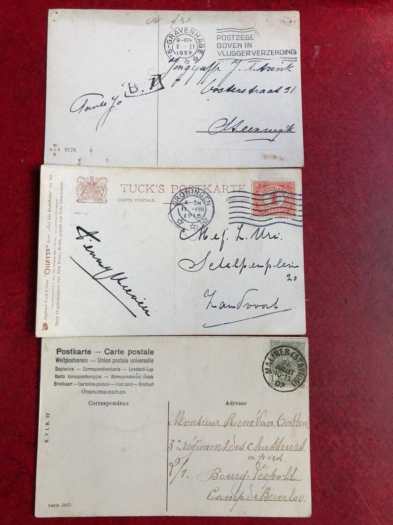 May include: Three vintage postcards with handwritten messages. The top postcard has a red stamp with the text "POSTZEGE BOVEN IN VLUGGER VERZENDING". The middle postcard has a red stamp with the text "TUCK'S POSTKARTE". The bottom postcard has a red stamp with the text "MALINES STATION 26 JUILLET 10-11 107".