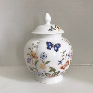 May include: A white porcelain jar with a lid, decorated with a floral pattern and butterflies. The jar has a round body and a slightly flared base.