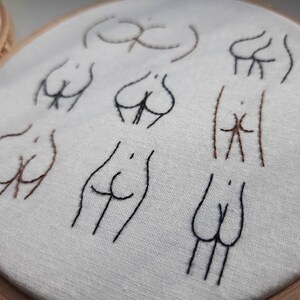 May include: Embroidered hoop art with multiple stylized figures in black and brown thread on a white fabric background.