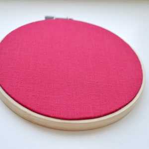 May include: A round embroidery hoop with a bright pink fabric stretched across the frame.