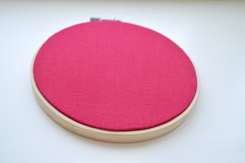 May include: A round embroidery hoop with a bright pink fabric stretched across the frame.
