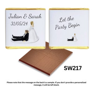 May include: Two white chocolate squares with gold foil wrappers. The front square has a personalised message that says "Julian & Sarah 31/05/24" and a cartoon image of a bride and groom. The back square has a cartoon image of a bride and groom and the text "Let the Party Begin". The chocolate squares are sitting on top of a brown chocolate bar with a grid pattern. The chocolate bar has the text "SW217" printed on it.