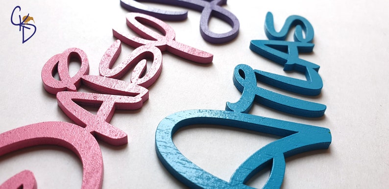 May include: Three wooden names, "Casey", "Elle", and "Ava", are painted in pink, purple, and teal.