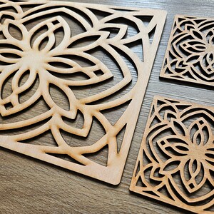 May include: Three wooden coasters with intricate laser-cut designs. The coasters feature a repeating pattern of geometric shapes and floral motifs. The coasters are made of light brown wood and have a natural finish.